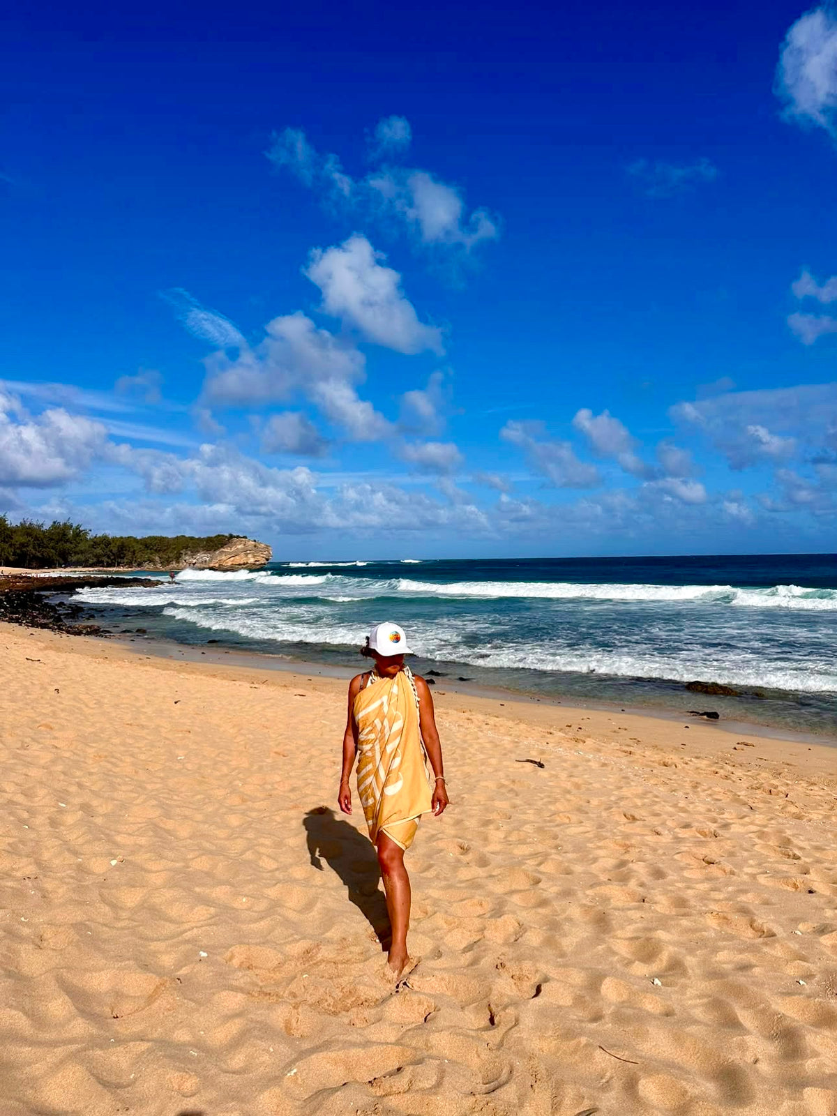 Person wrapped in Golden Hour Turkish cotton beach towel walking along a sandy beach in Hawaii