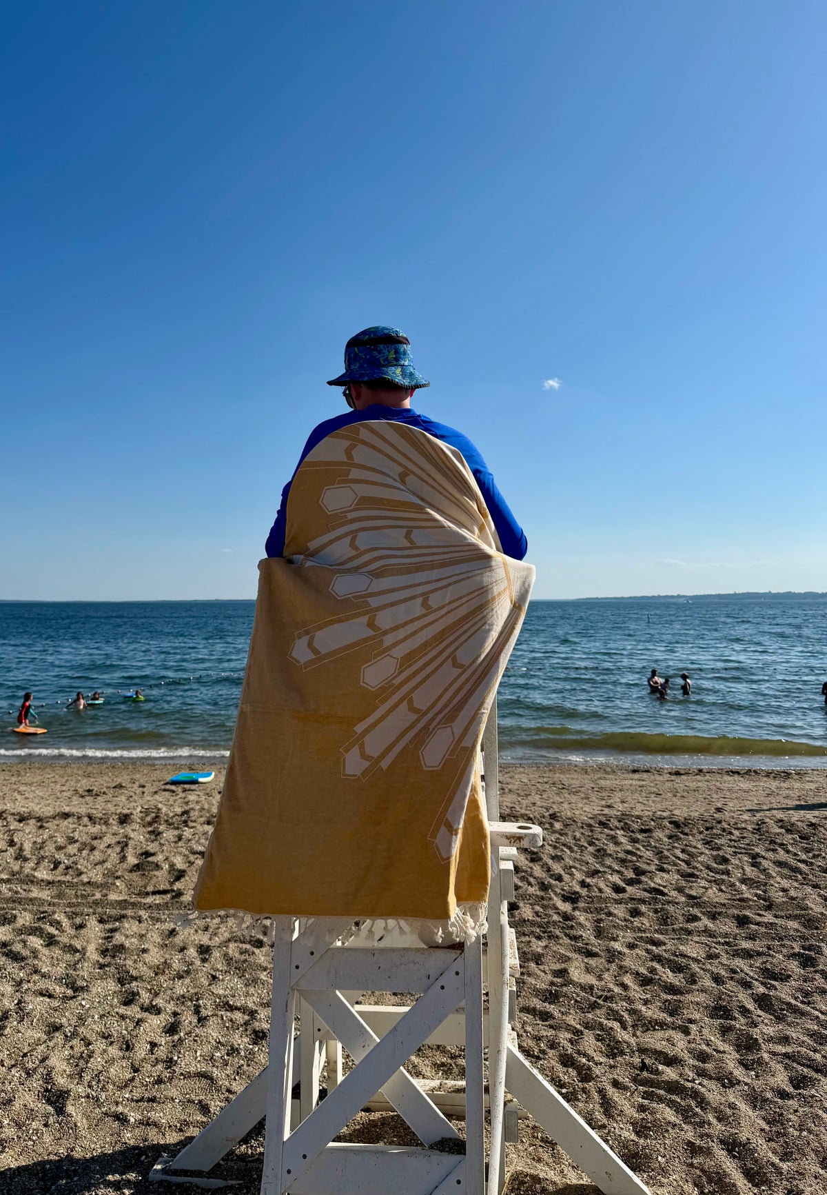 Person wrapped in Deco Sunburst Turkish cotton beach towel on a lifeguard chair at Barrington Beach in Rhode Island