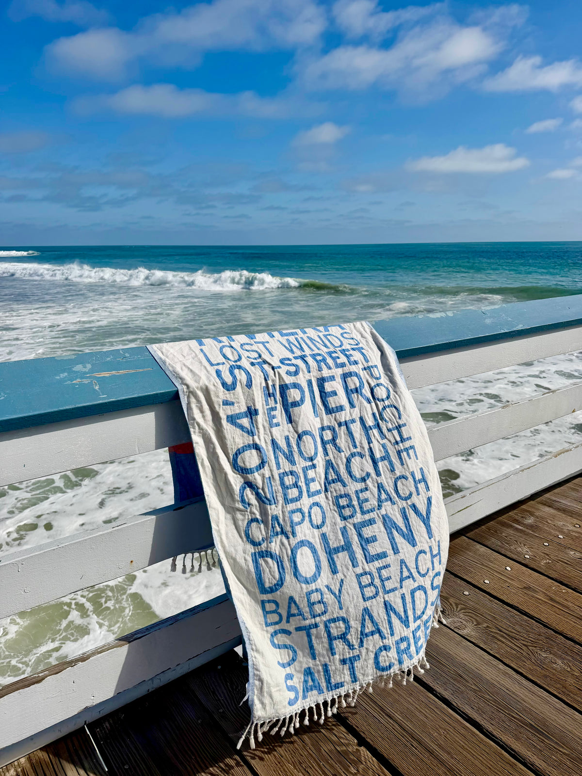 South OC Beaches Turkish cotton beach towel draped on a boardwalk railing overlooking the ocean