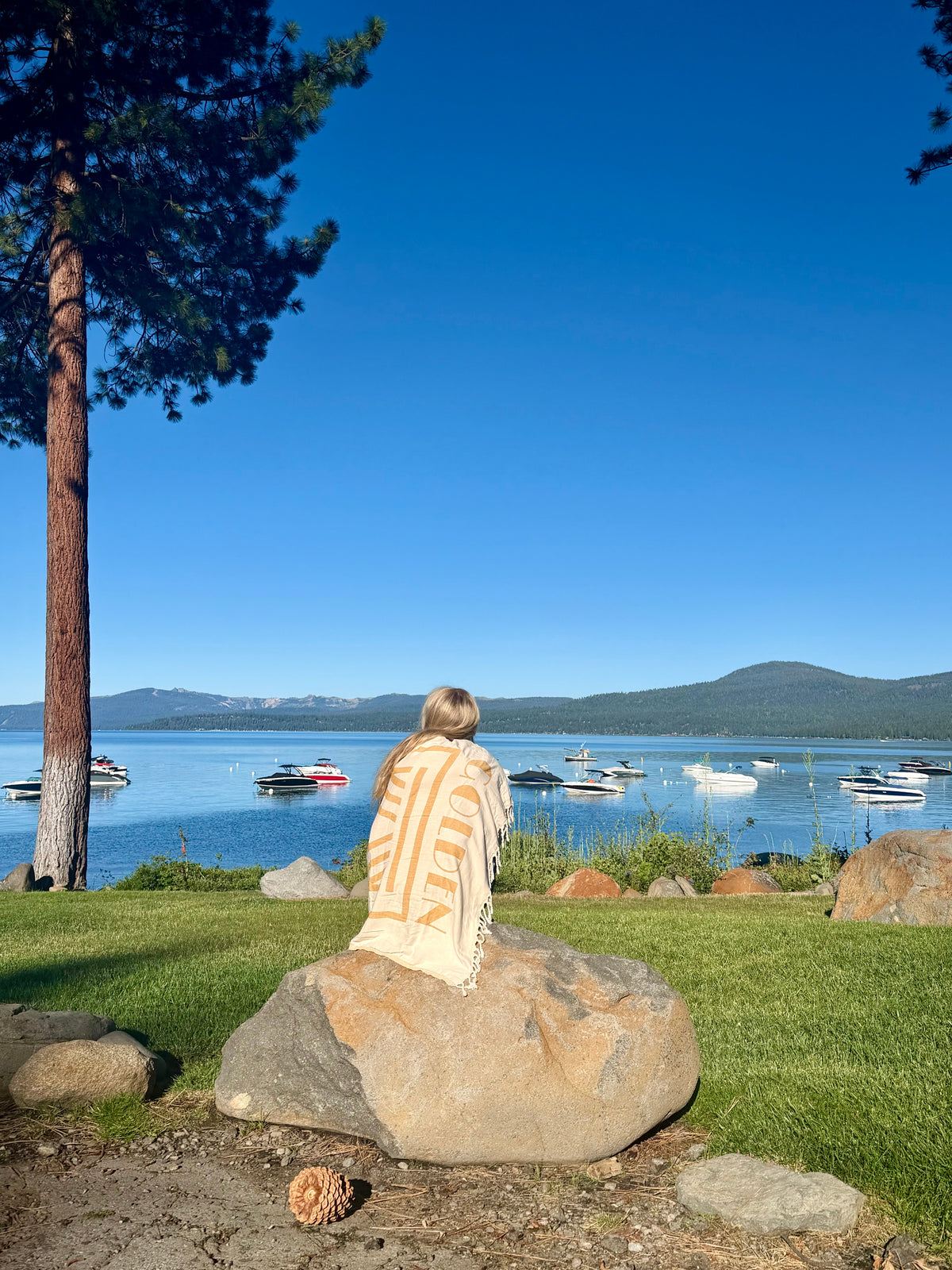 Person wrapped in Golden Hour Turkish cotton beach towel sitting by the water