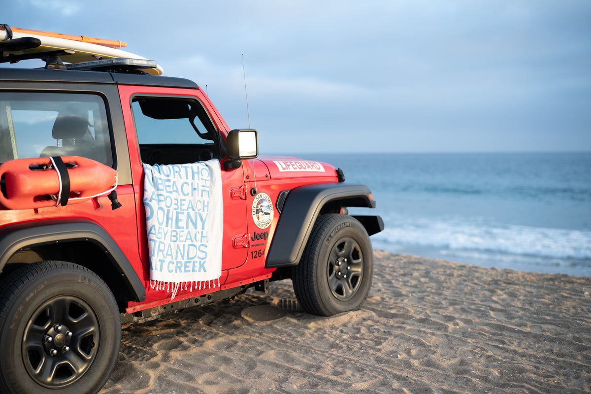South OC Beaches Blue Turkish cotton beach towel draped on a red Jeep at the beach